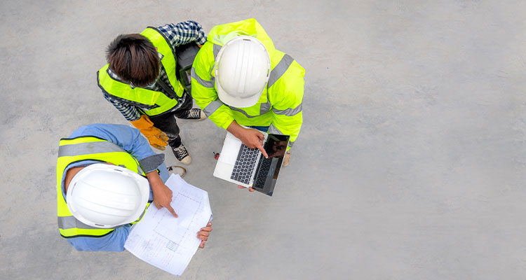 Overhead shot of 3 builders looking at laptop & architects drawing